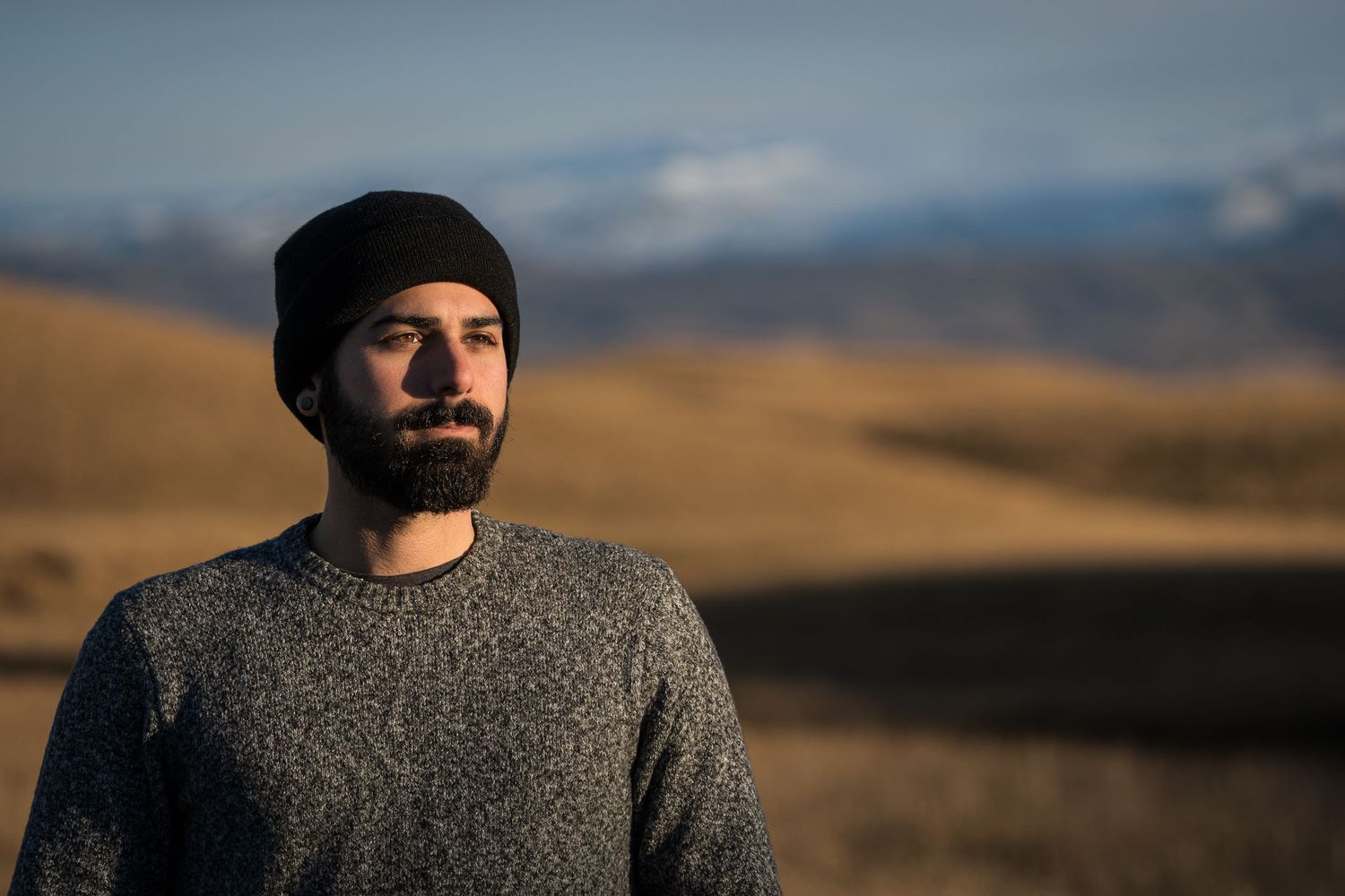 Portrait of person in knit beanie and sweater with mountainous landscape behind them.