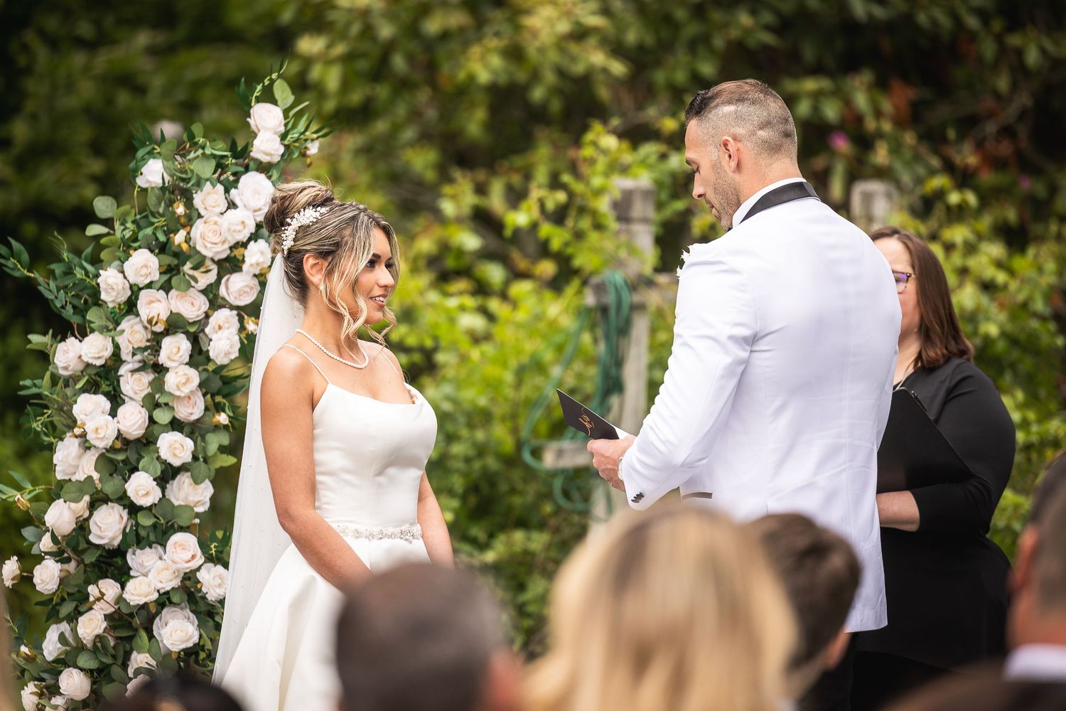 Outdoor wedding ceremony with floral arrangements and guests in a garden setting.