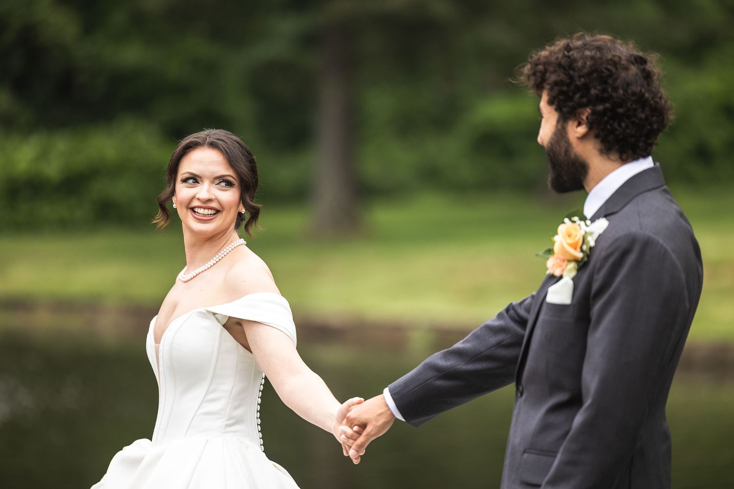 Happy couple sharing joyful moment by lakeside in wedding attire.