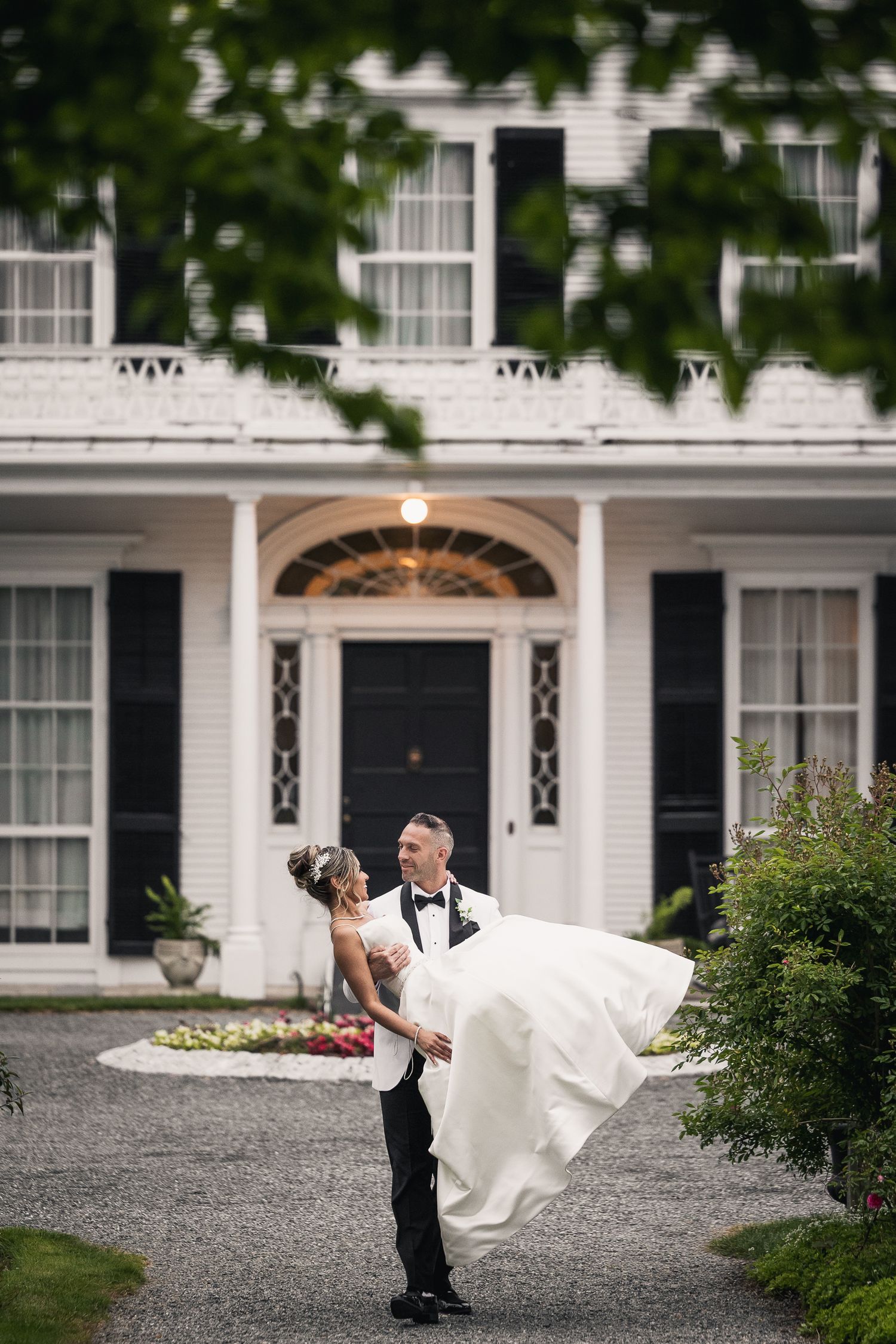 Romantic wedding couple poses in front of a grand white colonial-style mansion.