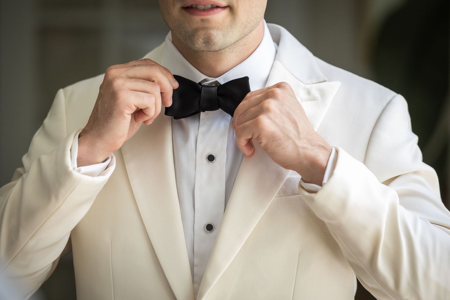 Person adjusting bow tie while wearing crisp white formal jacket.