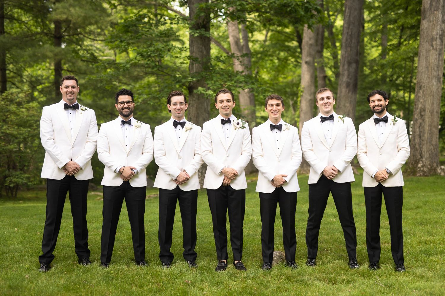 Groomsmen in black and white attire sitting on grass in a garden.