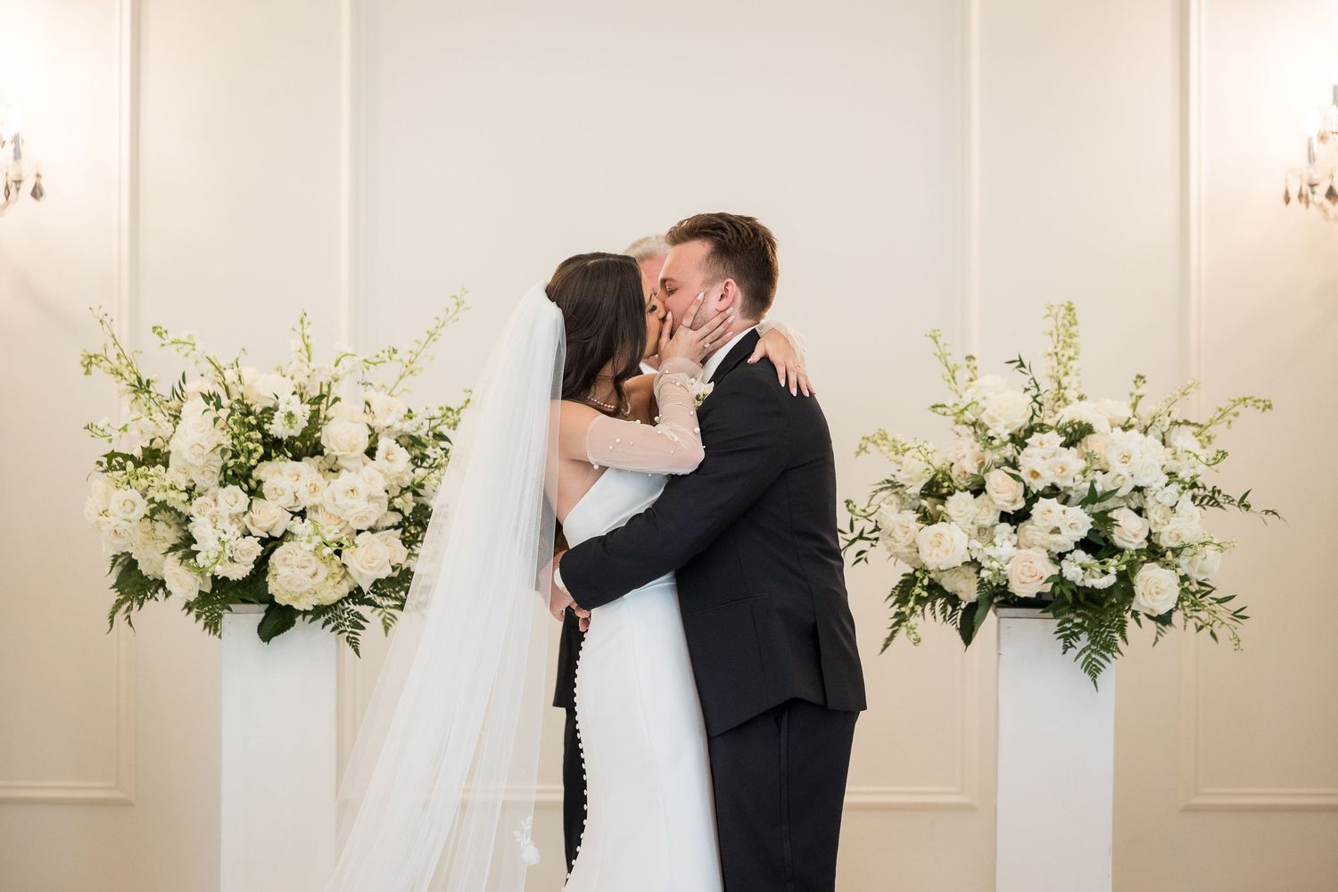 Elegant wedding couple sharing romantic moments against a backdrop of white floral arrangements and chandeliers.