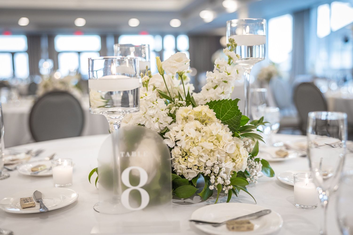 Elegant wedding reception table settings with white floral centerpieces and crystal glassware.