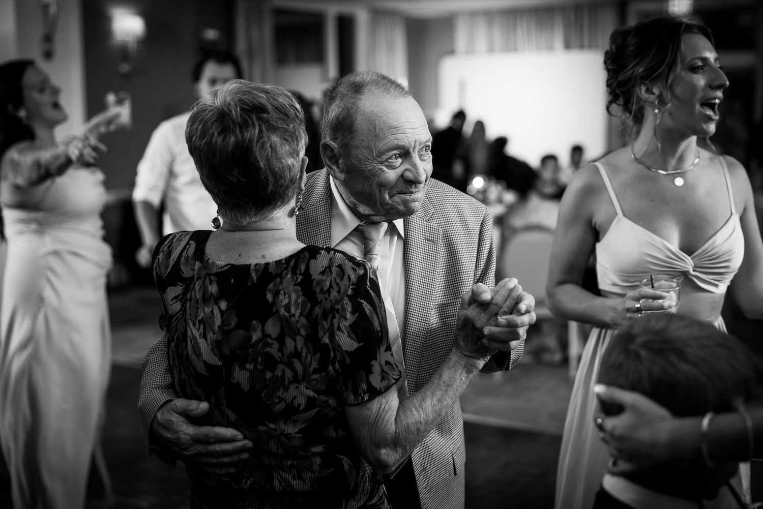 Black and white candid dance floor moments at an indoor celebration.