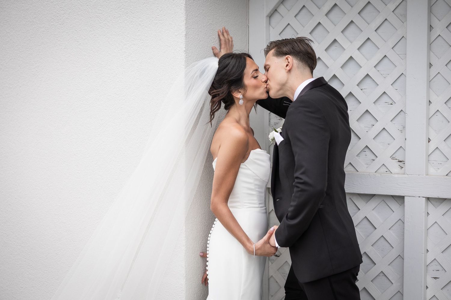 Romantic wedding couple embraces against white lattice backdrop in black and white.
