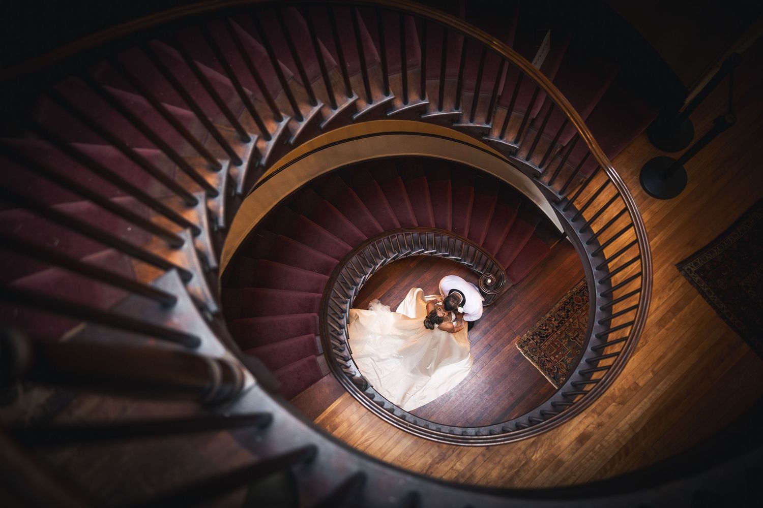A spiral wooden staircase photographed from above creates a mesmerizing geometric pattern in warm lighting.