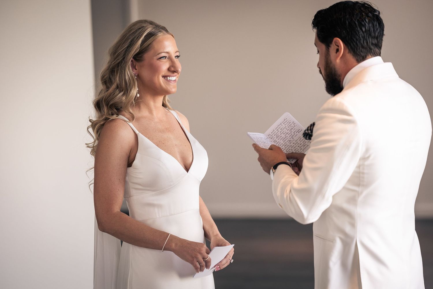 A couple in white attire exchange vows during an intimate wedding ceremony indoors.