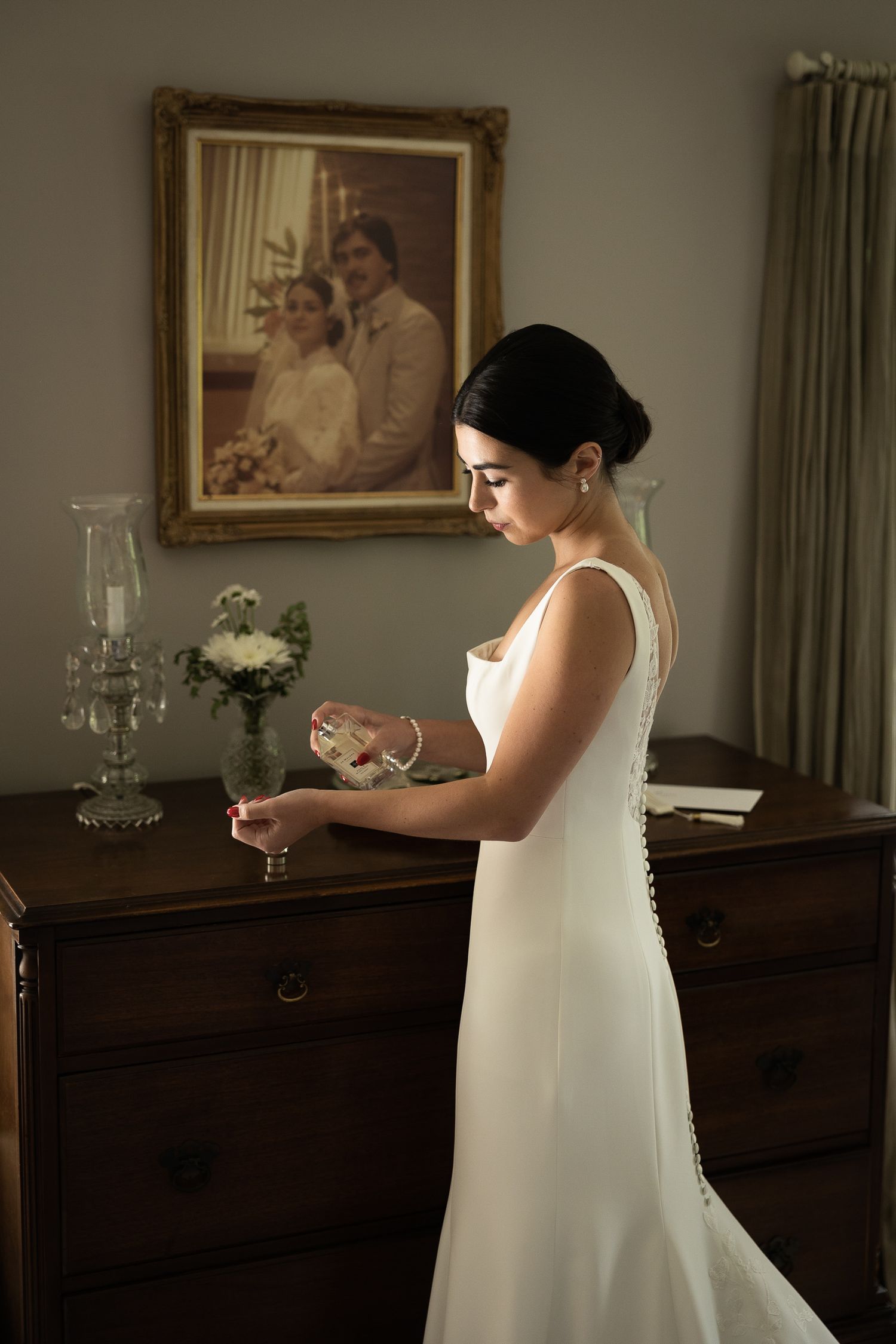 Bride in elegant white dress preparing in a room with classic furniture and artwork.