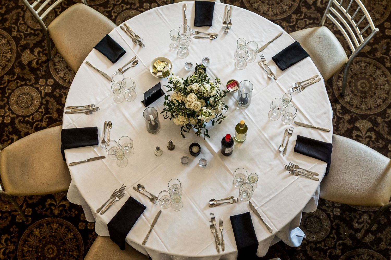 Overhead view of elegant wedding reception table settings with white linens and black accents.