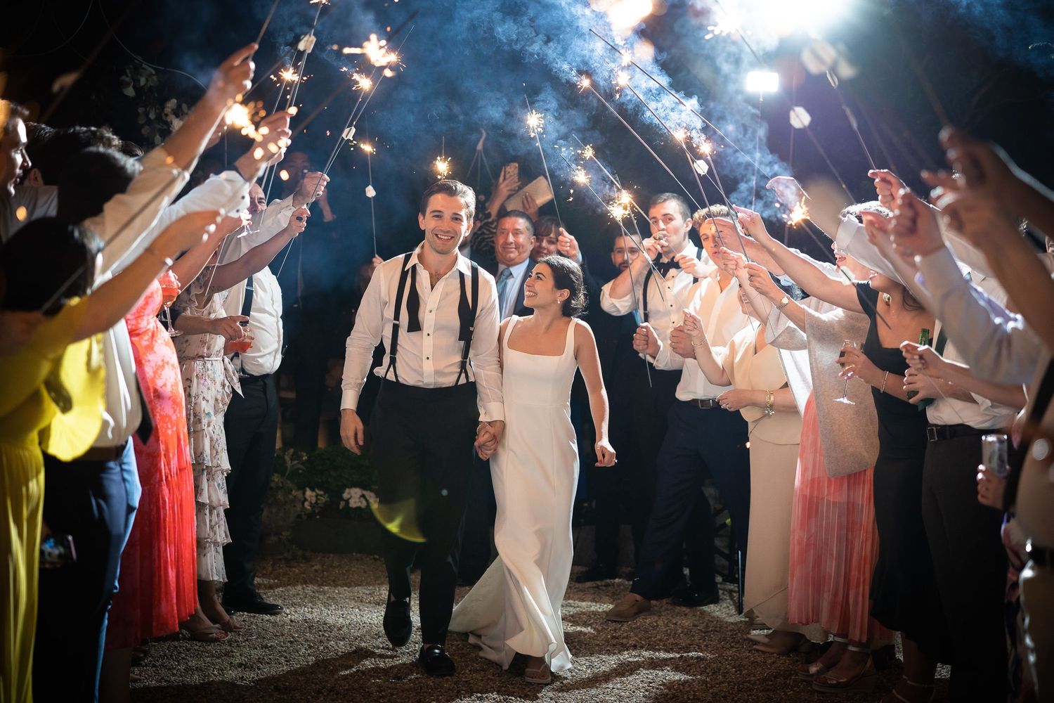 Wedding guests form a sparkler exit tunnel for the newlyweds under the night sky.