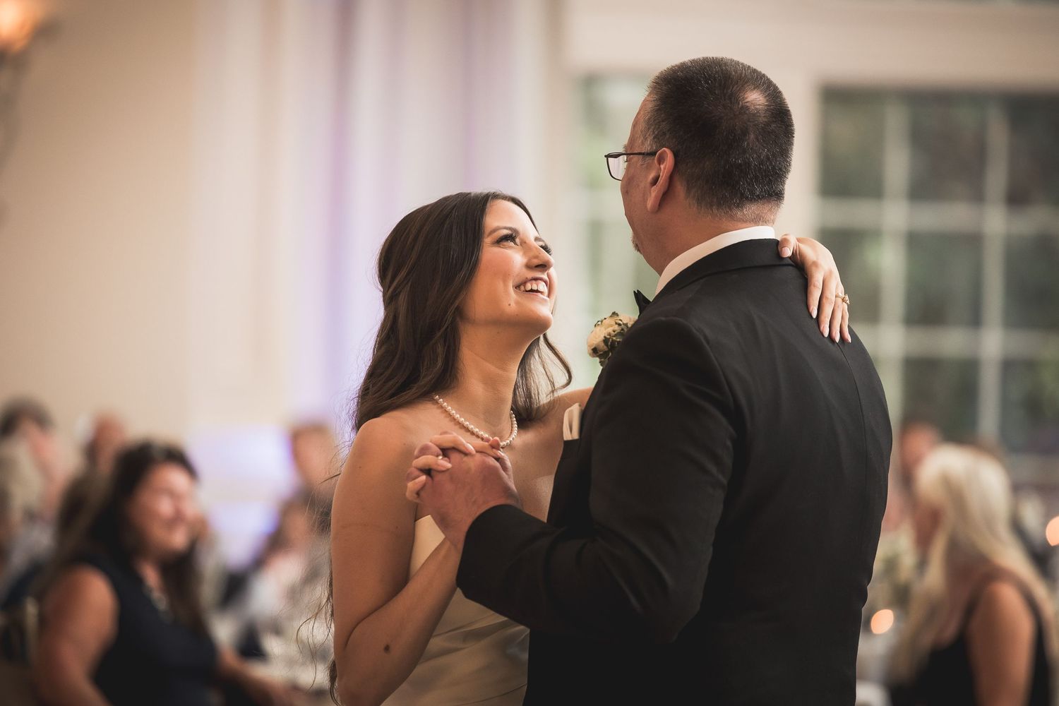 Romantic first dance between newlyweds in an elegant ballroom with chandelier lighting.