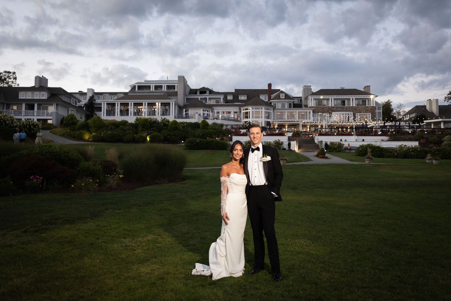Wedding couple poses on lawn with grand coastal estate building in background.