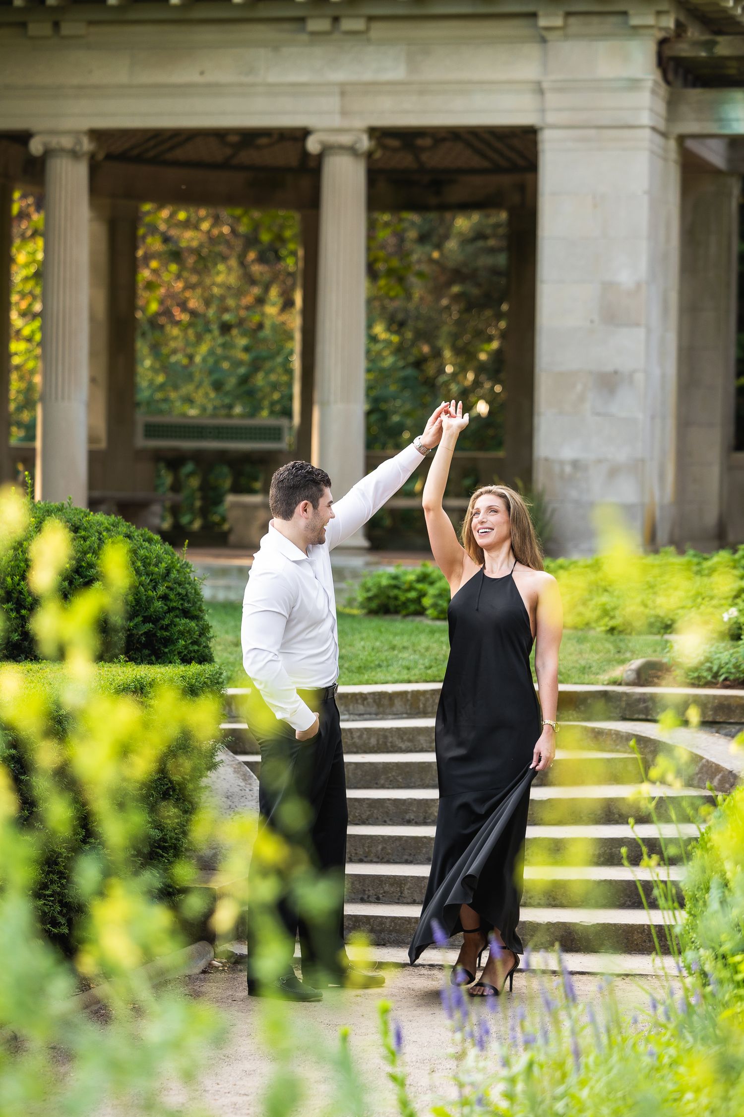 Two people high-five each other while standing on stone steps in a garden setting with greenery in the background.
