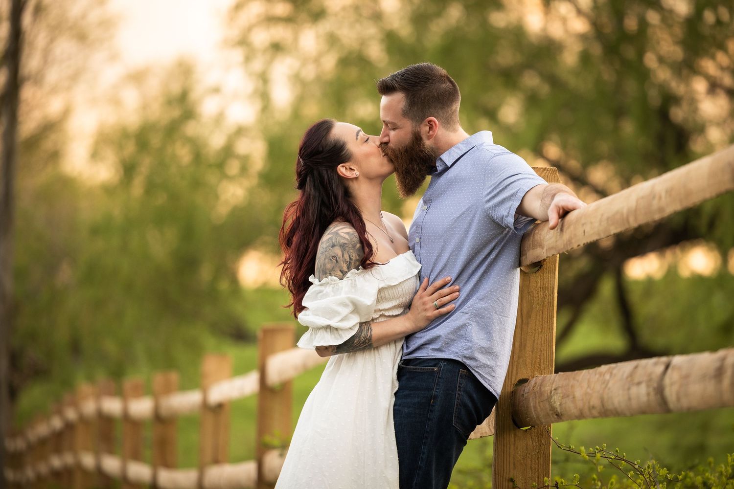 A romantic couple shares tender moments together against a rustic wooden fence in golden evening light.