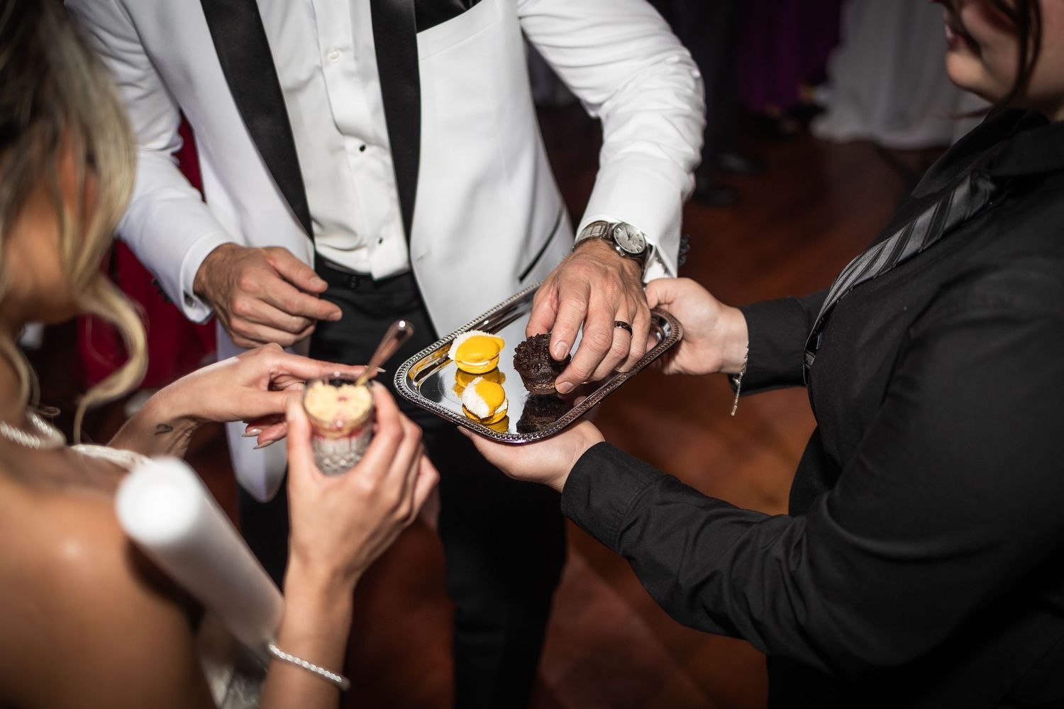 Servers in white uniforms presenting hors d'oeuvres on silver platters at an elegant event.