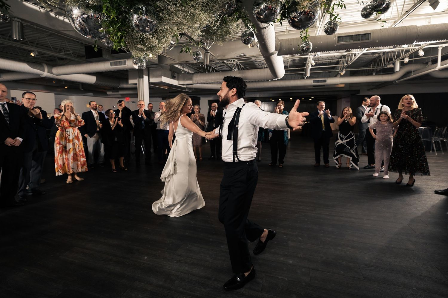 Wedding guests dance together on a dark dance floor during an evening reception celebration.