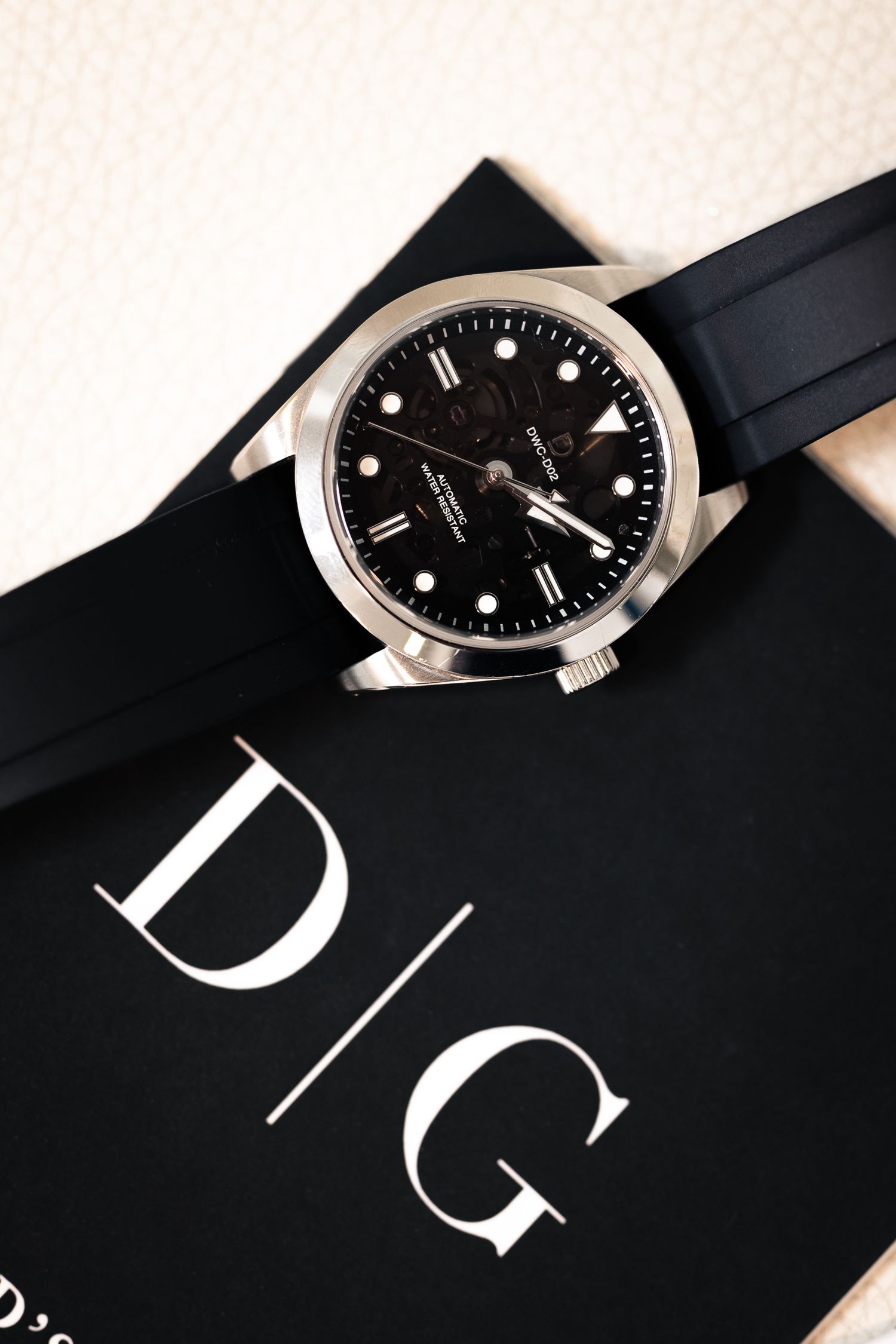 Close-up view of a luxury watch with black dial and rubber strap against dark background creating minimalist composition.