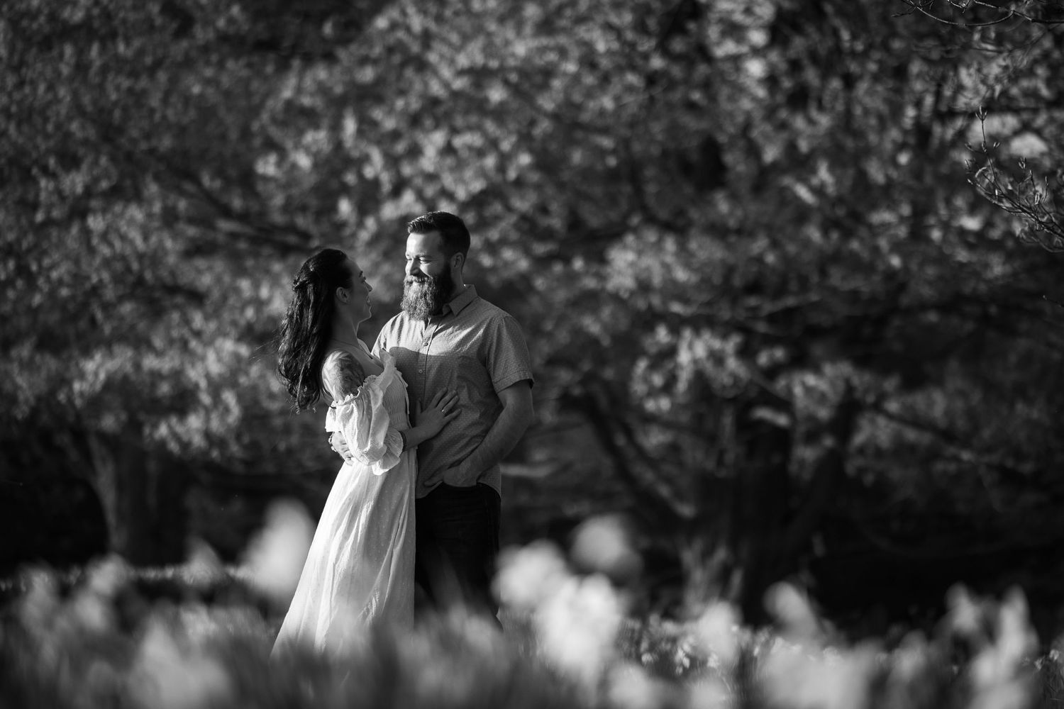 A black and white photo series shows a romantic couple walking through a garden setting with cherry blossoms.