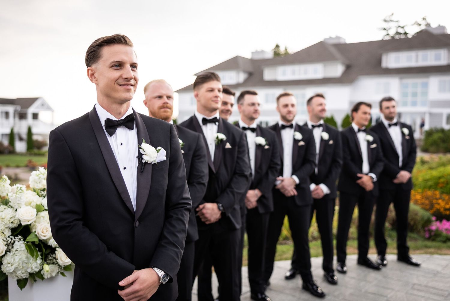 Groomsmen in classic black tuxedos lined up for formal outdoor portrait.