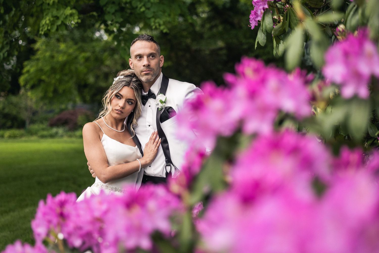 Romantic wedding portraits in a garden with vibrant pink flowers in the foreground.