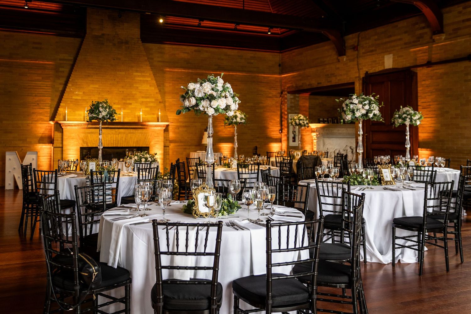 Wedding reception venue with elegant table settings and black chiavari chairs in warm wooden room.