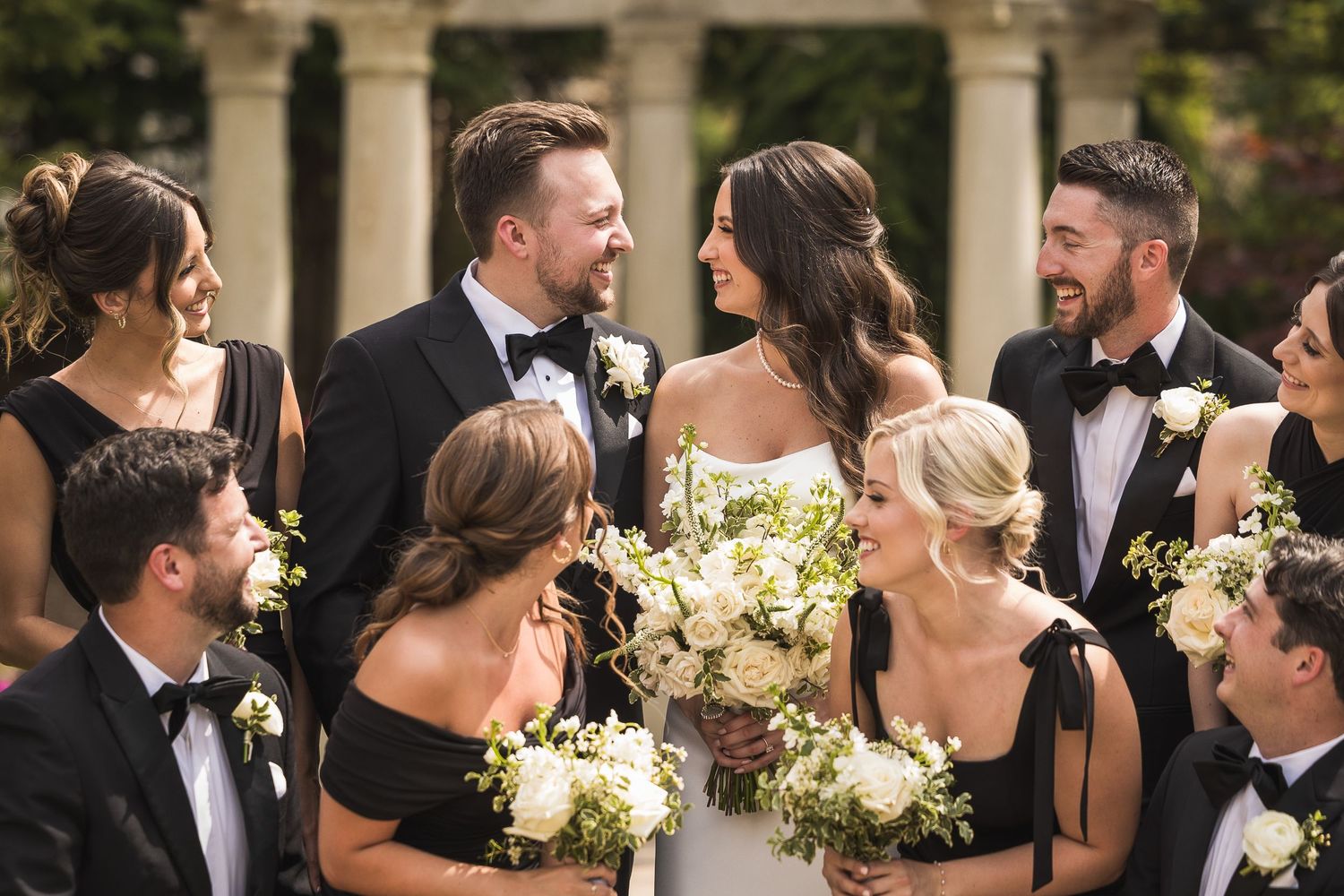 Wedding party posing together in formal attire with white floral bouquets.