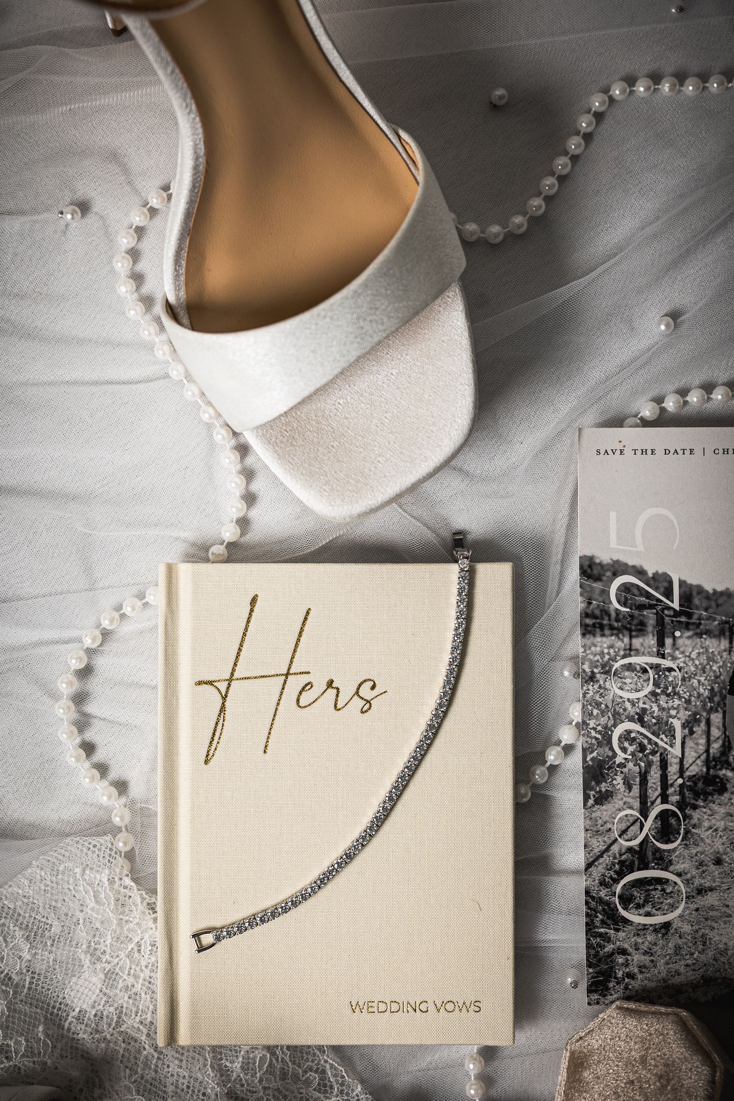 Wedding details flatlay with white shoes, pearl necklace and 'Hers' vow book.
