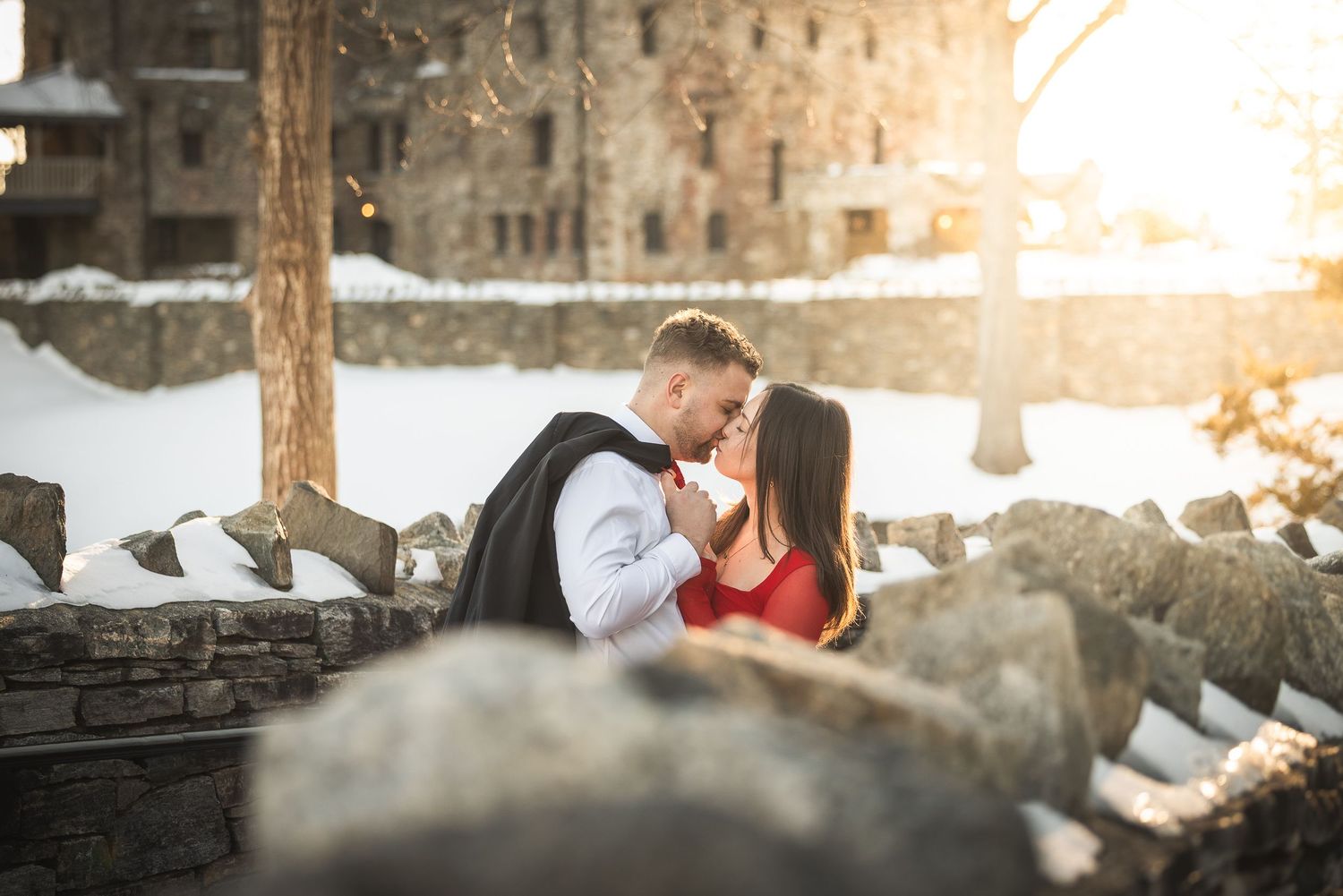 A couple poses together in a snowy winter setting during a romantic outdoor photo session at sunset.