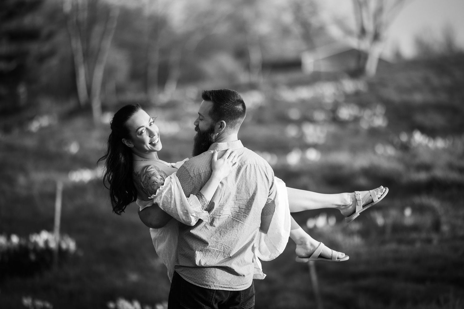 A romantic black and white portrait of a couple embracing outdoors, with the man holding the woman in his arms.