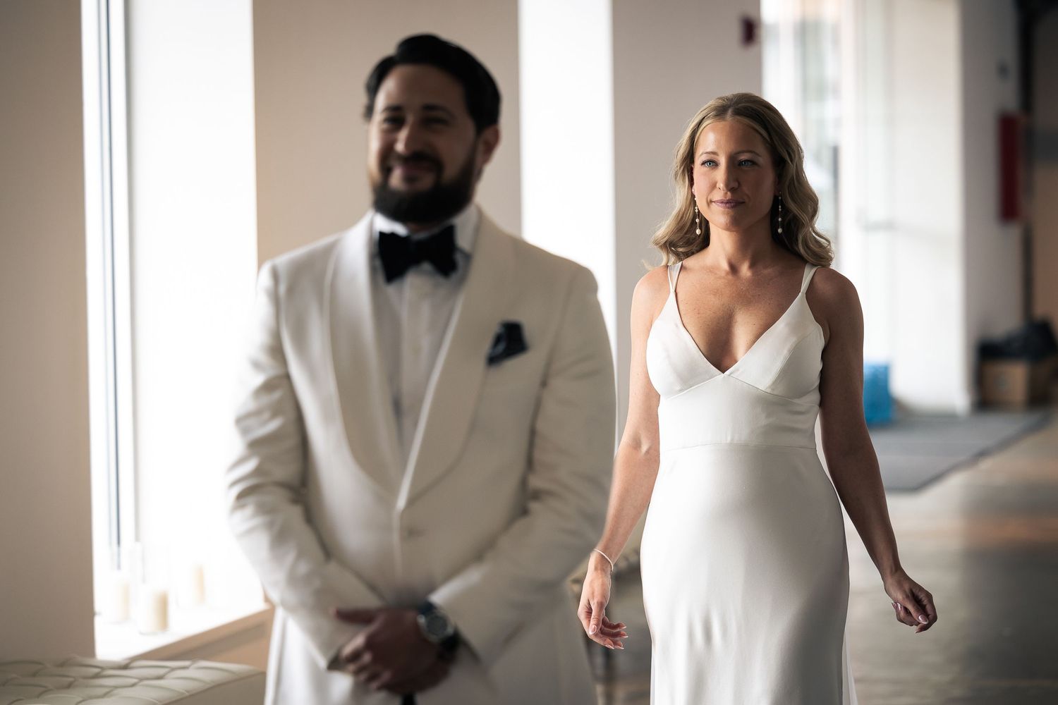 A wedding party in formal white attire poses together in a bright indoor venue.