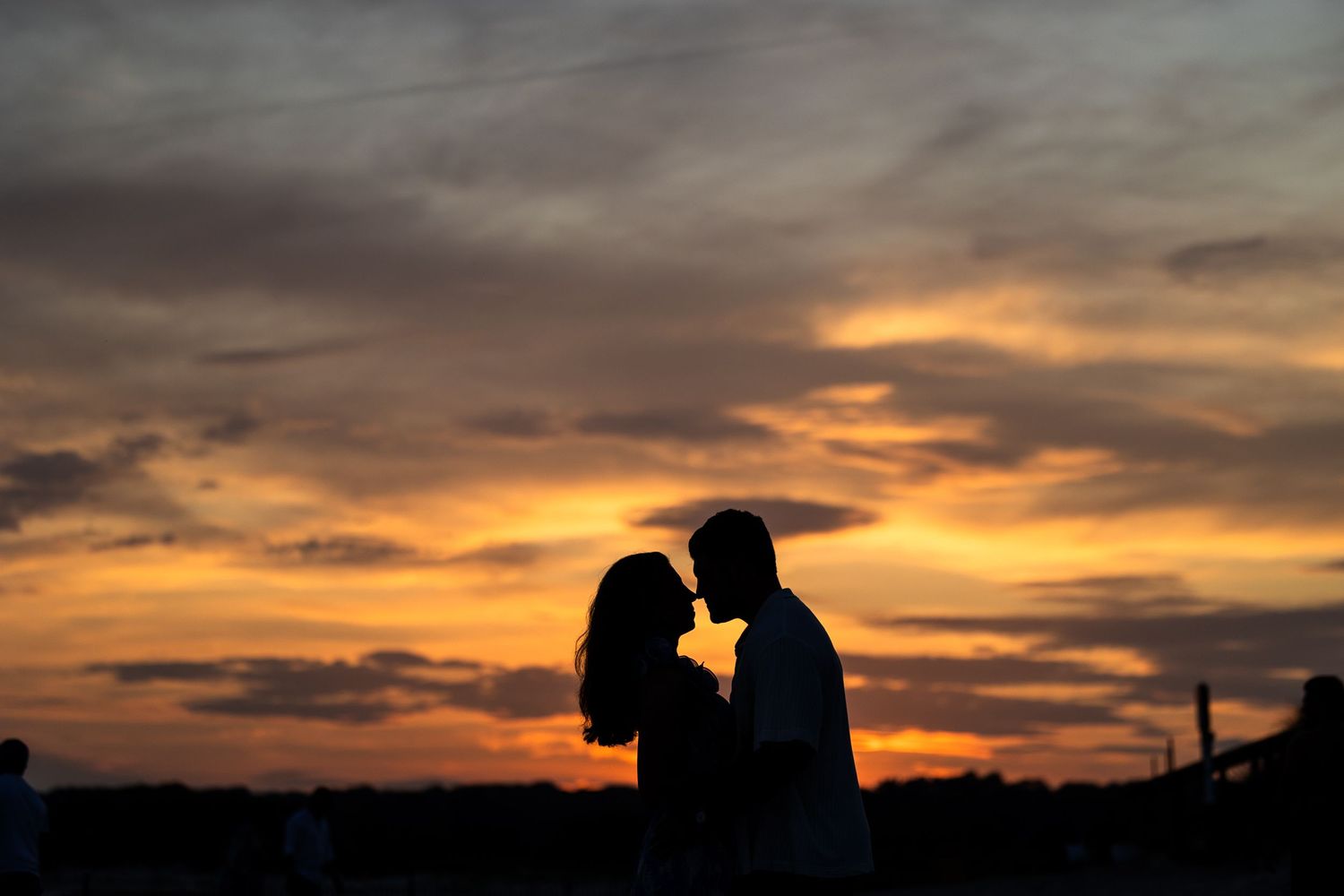 A romantic silhouette of a couple embraces against a dramatic orange and purple sunset sky.