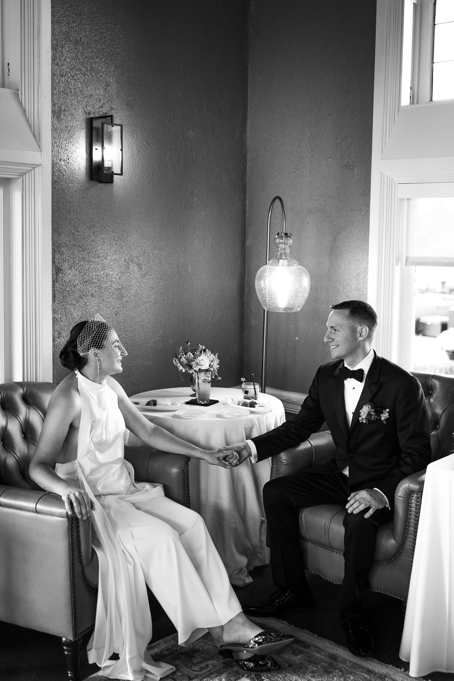 A black and white wedding photo series showing candid moments between a couple seated on a couch in a room.