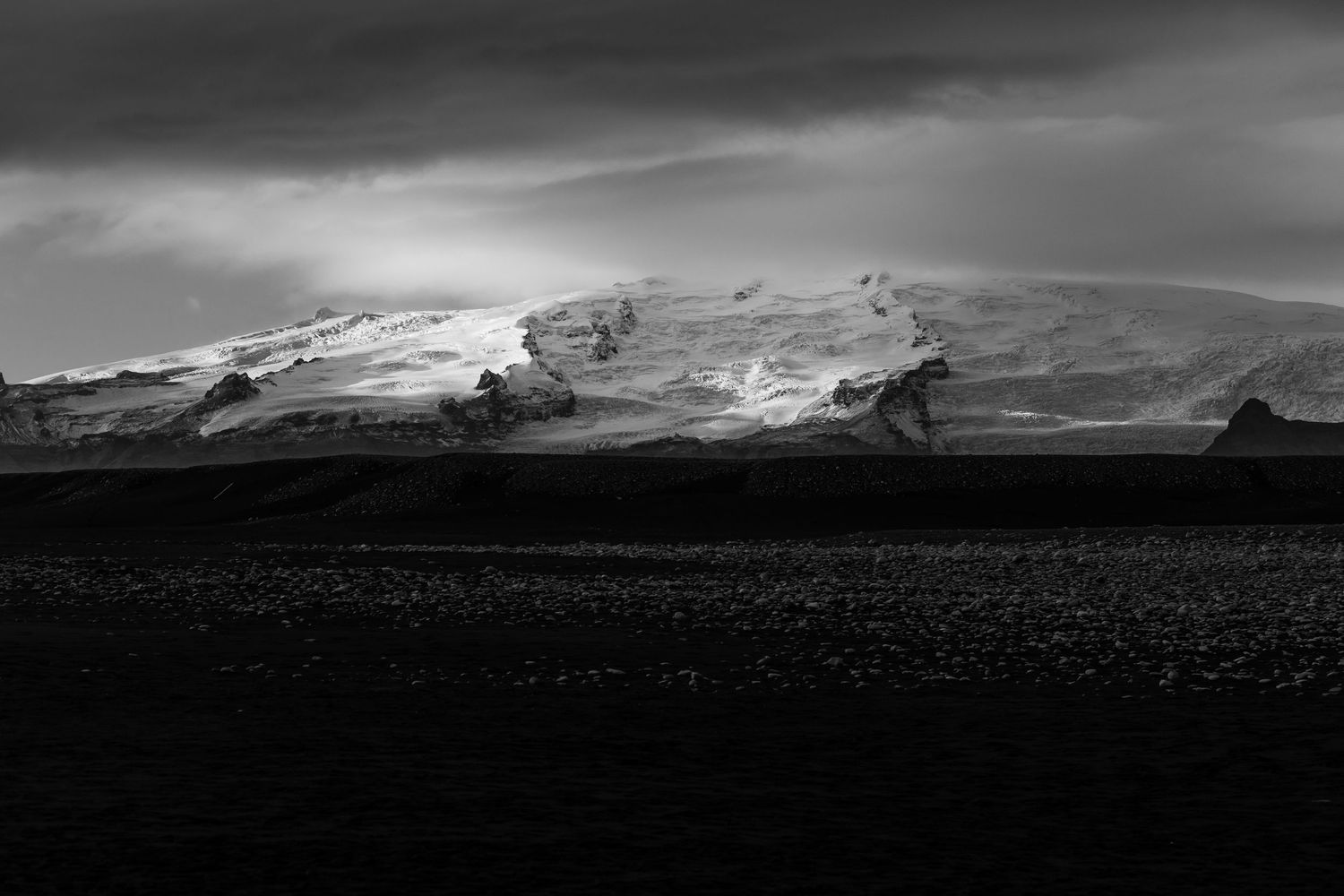 Black and white landscape of snow-capped mountains under moody sky.