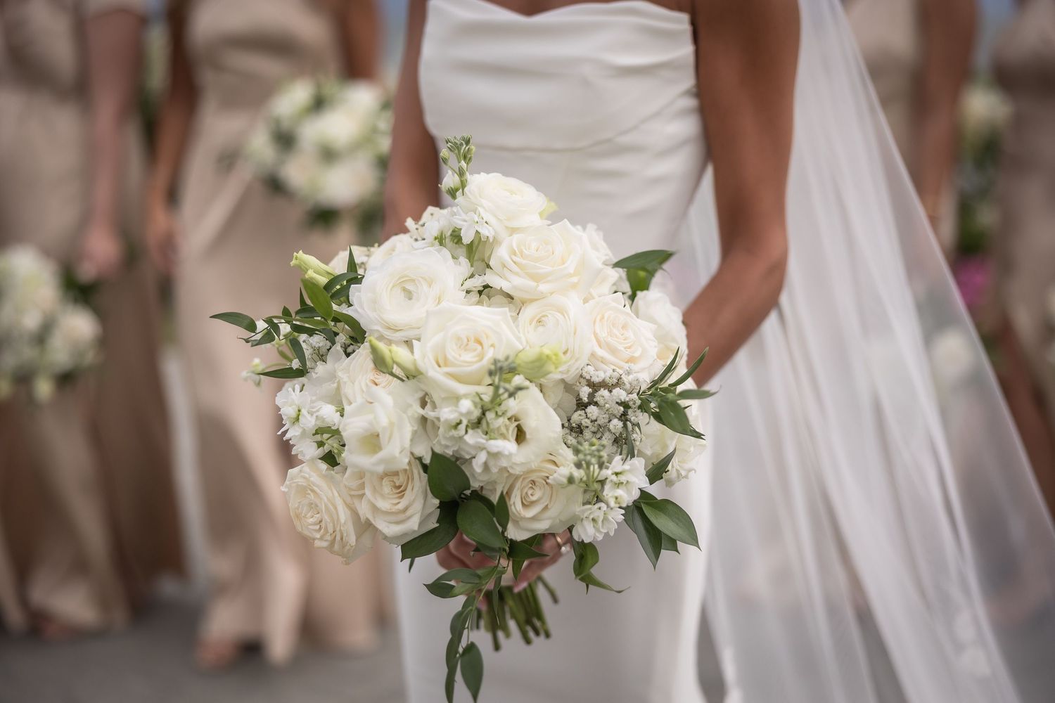 Close-up of white rose bridal bouquet held against a white wedding dress.
