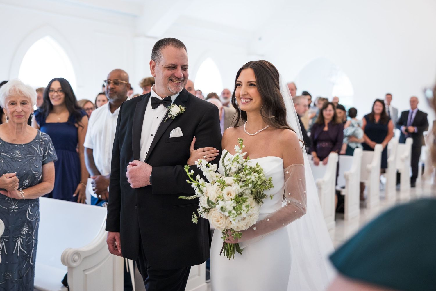 Wedding reception guests dancing and mingling in an elegant ballroom with crystal chandeliers.