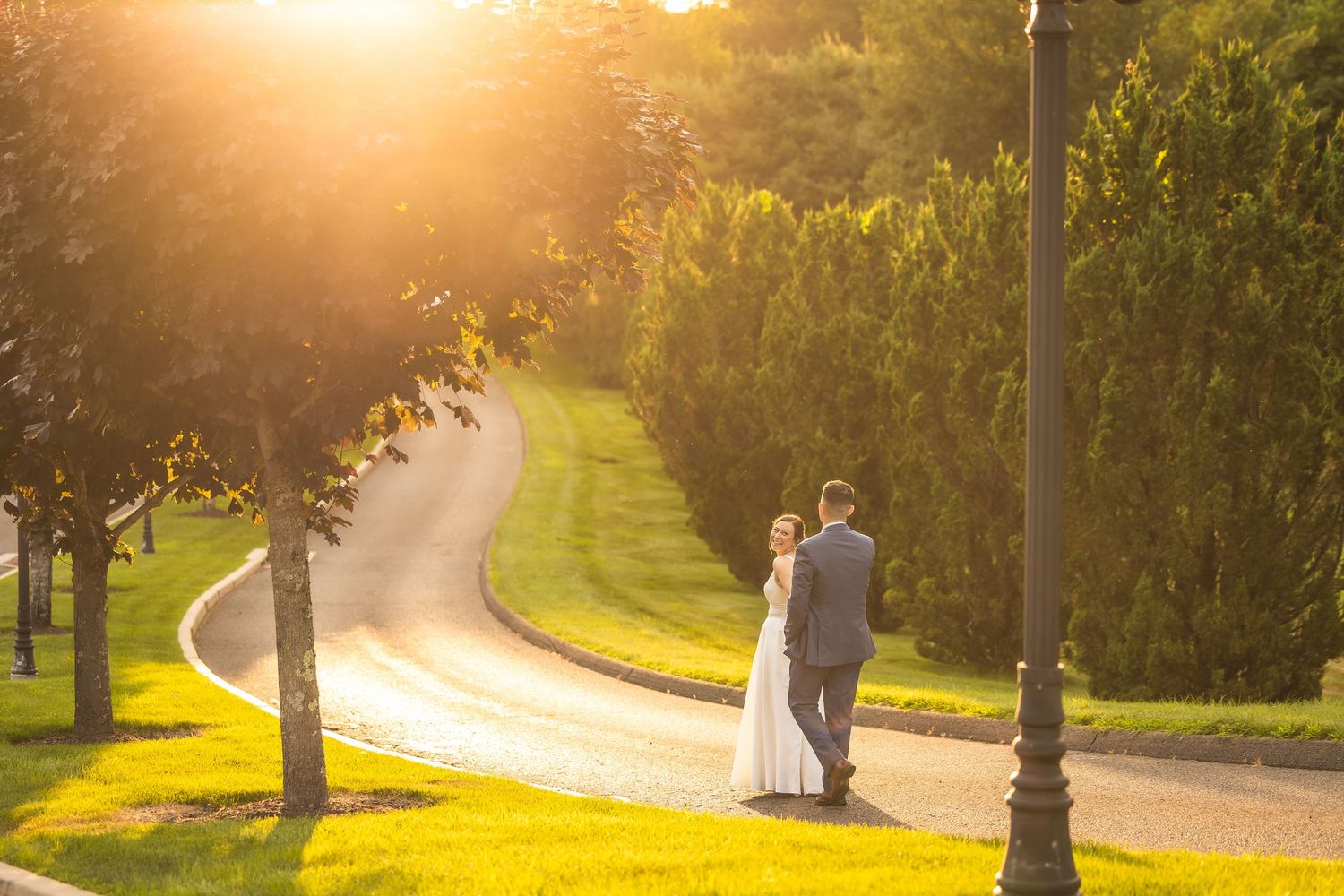 Golden sunlight streams through trees along a winding path in a park setting.