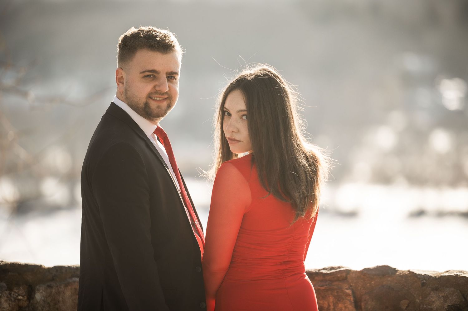 A couple in coordinating red and black outfits poses together in a romantic outdoor photoshoot at sunset.