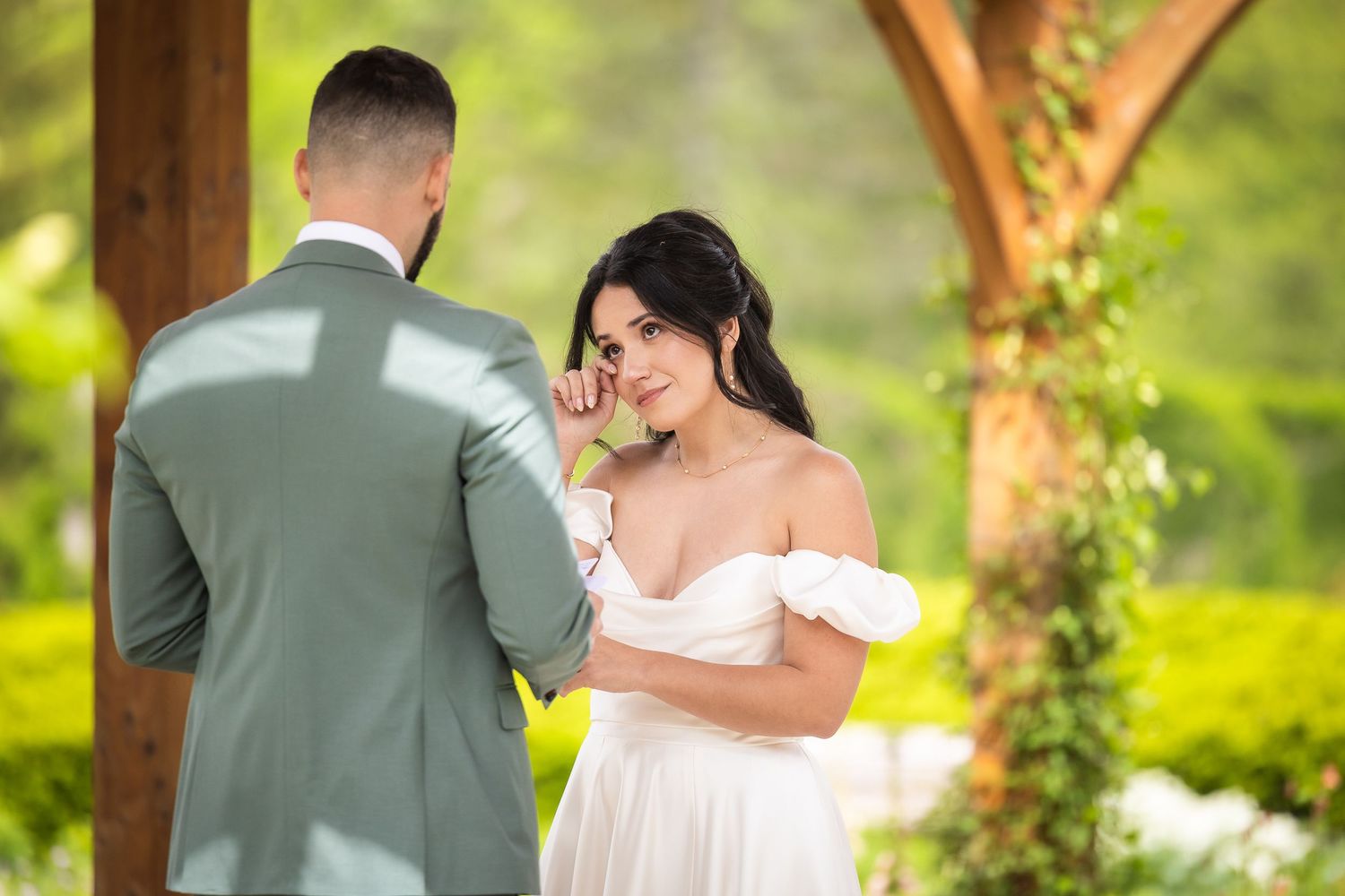 A romantic outdoor wedding ceremony with a couple embracing under wooden beams surrounded by lush greenery.