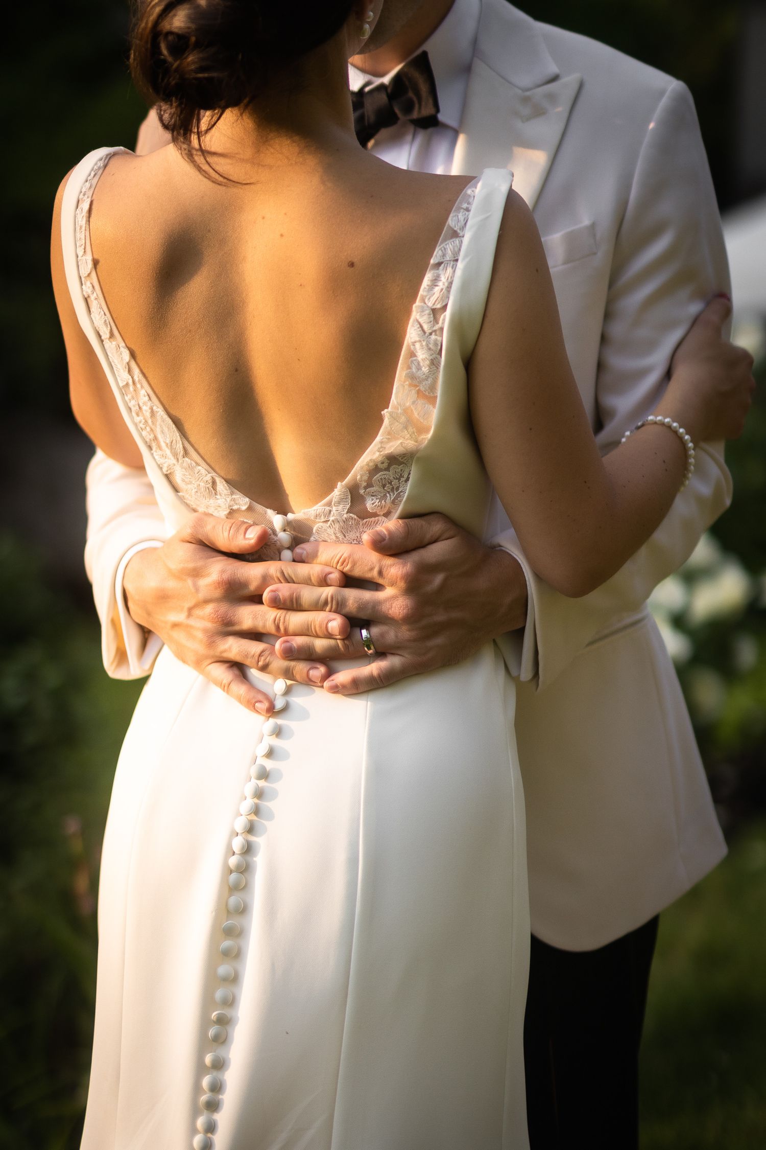 Close-up detail of wedding dress showing intricate lace back design and groom's hands.