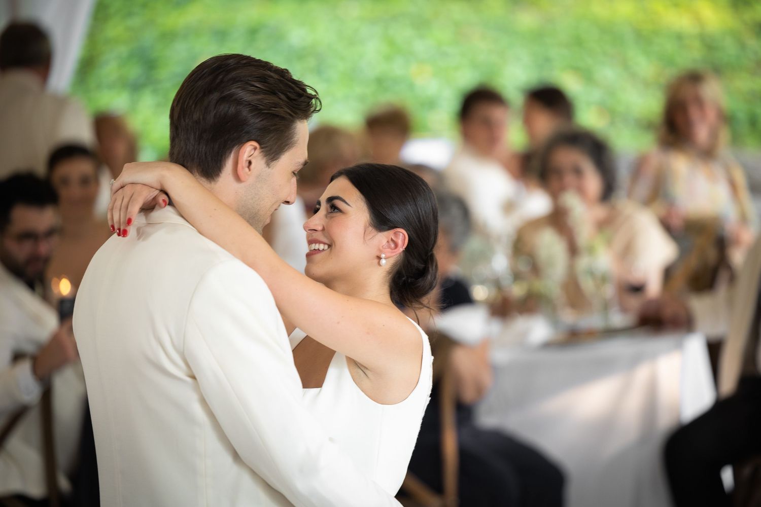 Couple shares their first dance at an outdoor wedding reception under a tent with guests looking on.