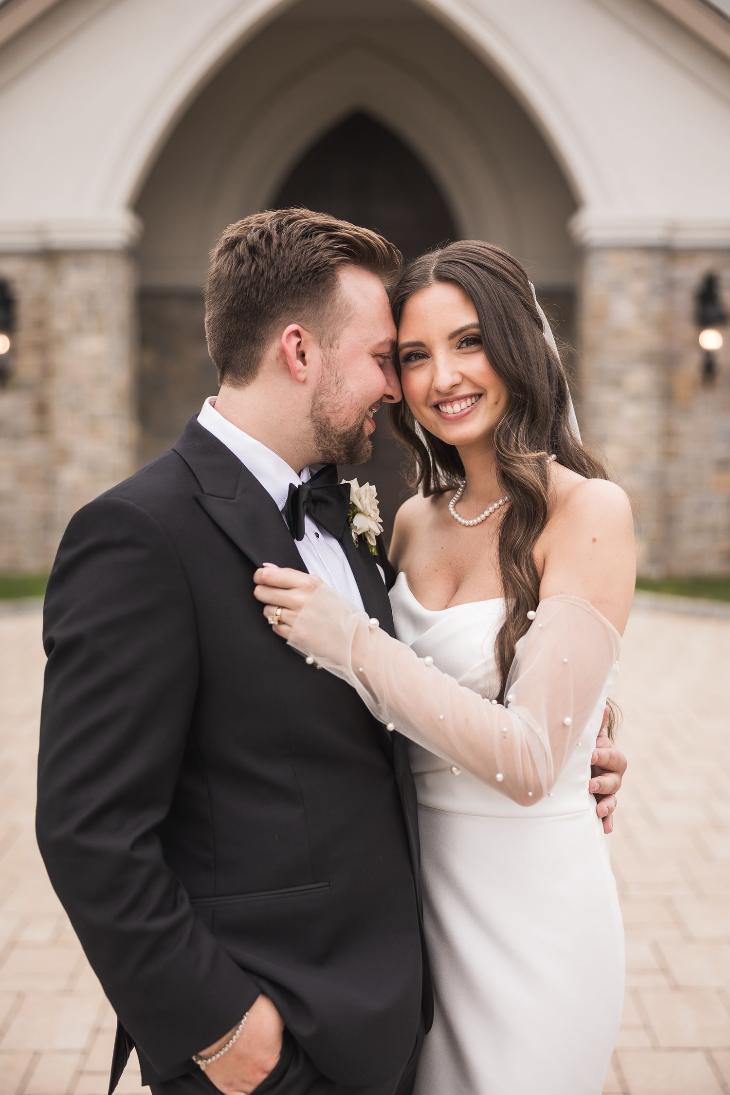 Romantic wedding couple embracing under stone archway.
