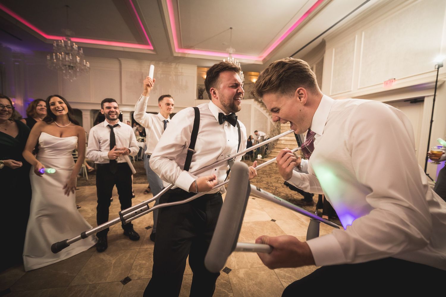 Wedding reception guests dancing and celebrating on the dance floor with colorful lighting.
