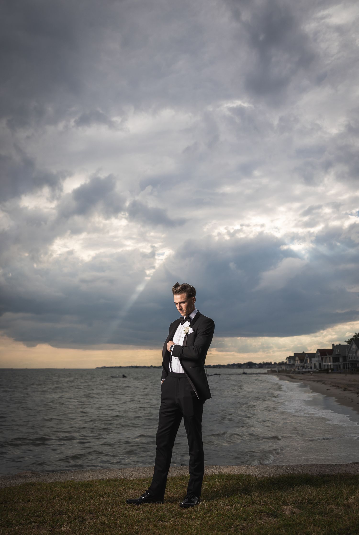 Dramatic portrait of groom in suit against stormy coastal sky.