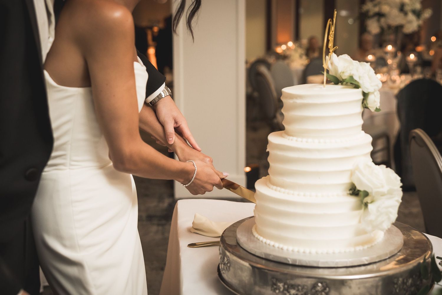 Classic white tiered wedding cake being cut during the reception.