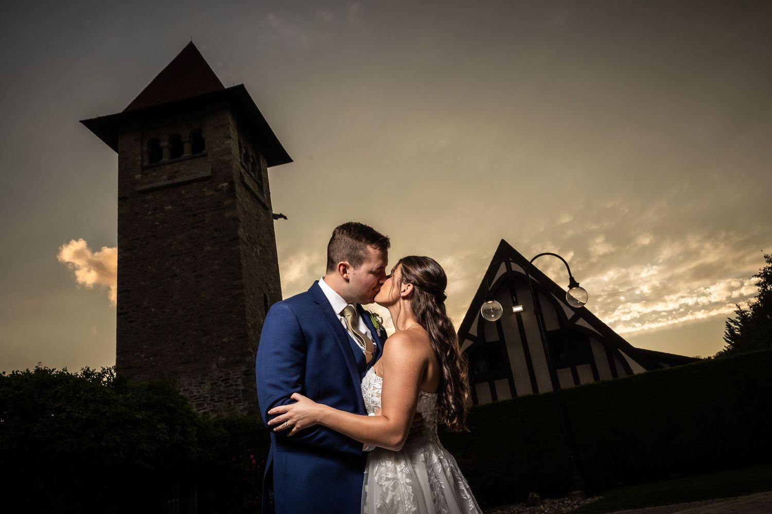 Silhouetted couple shares a romantic kiss against a dramatic sunset sky with a church tower in the background.