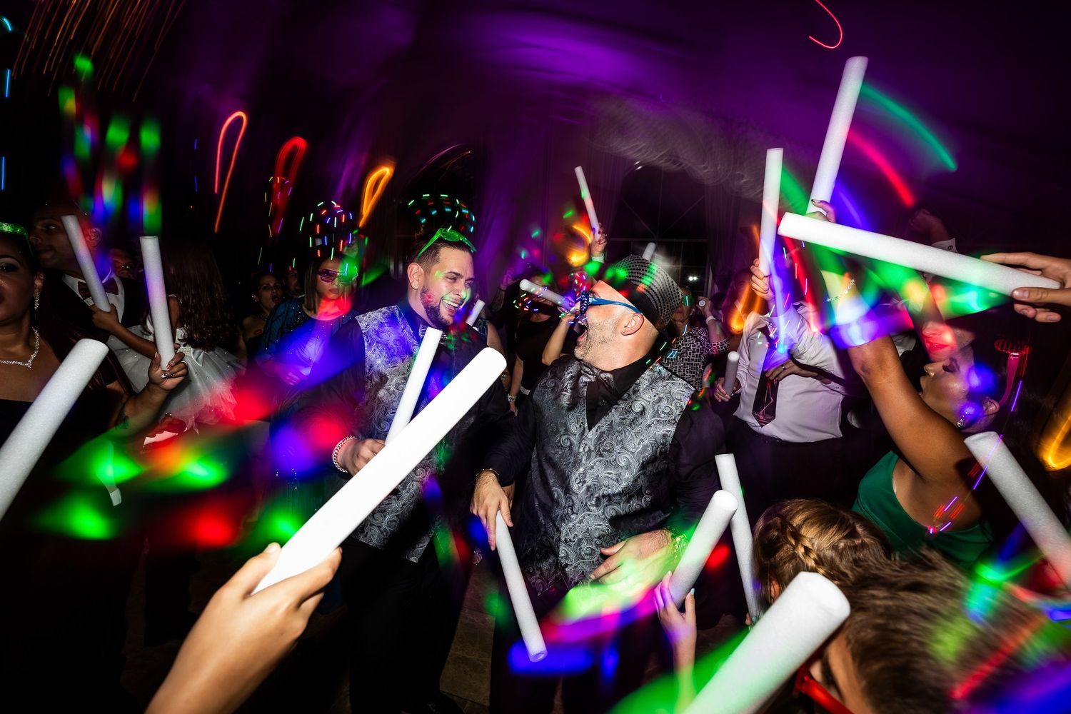 A crowd waves colorful LED light sticks at a nighttime concert or party event with purple lighting effects.