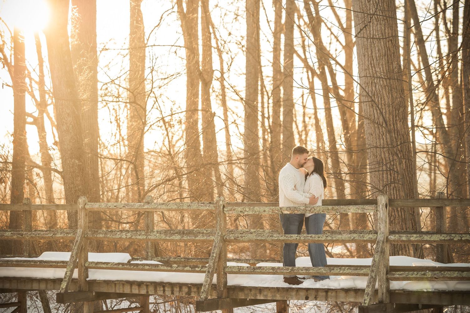 Wooden boardwalk trail winds through a misty forest during golden sunset with sunlight filtering through bare trees.