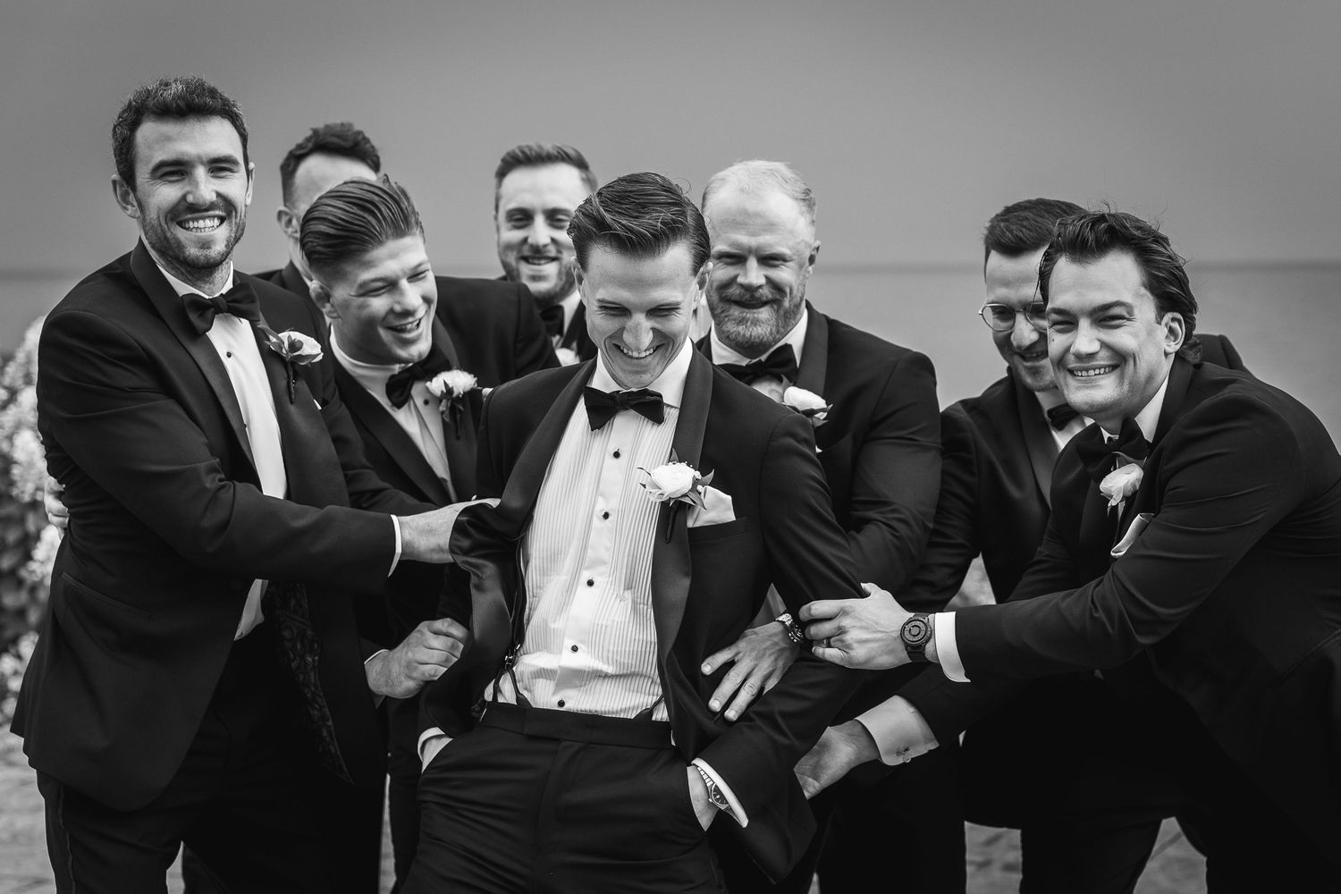 Groomsmen in black tuxedos share a candid laughing moment together.