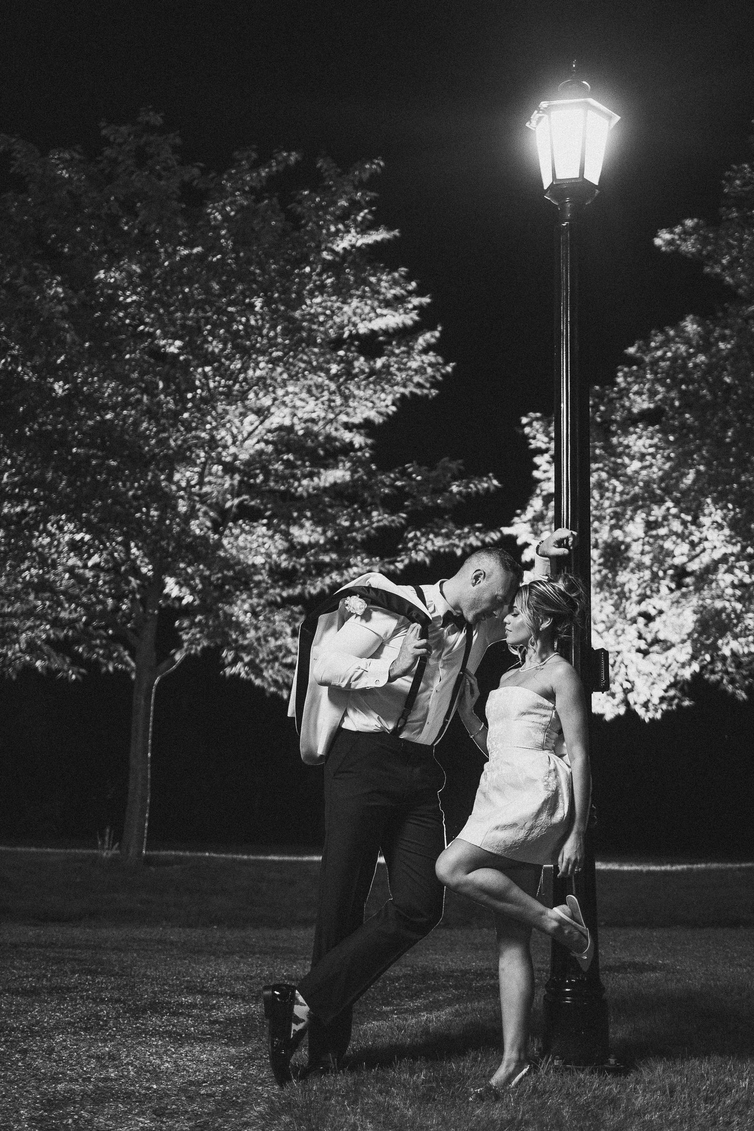 Romantic nighttime wedding portraits under vintage street lamps in a garden setting.